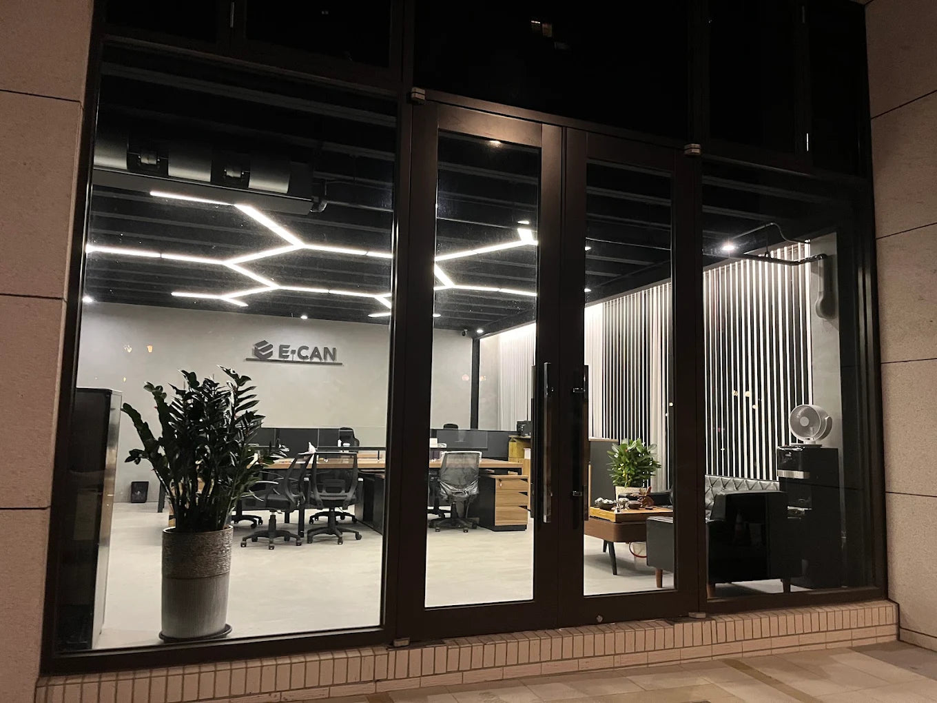 E-CAN office workspace seen through glass doors, with the E-CAN logo on the interior wall